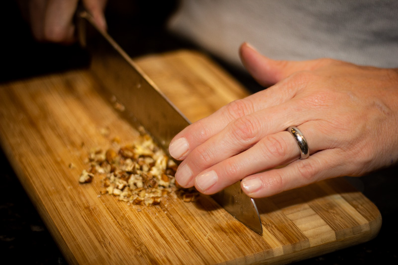 Closeup of a woman's hands chopping walnuts on a cutting board